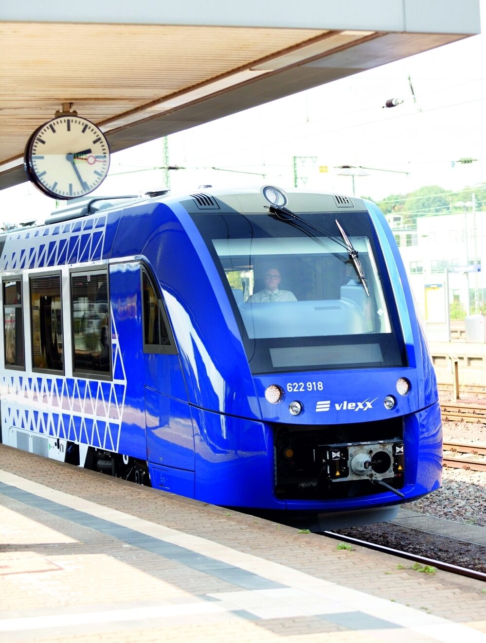 Ein blauer Zug von vlexx steht an einem Bahnhof an einem Bahnsteig. Darüber eine Uhr, die die Uhrzeit 14 Uhr 25 anzeigt.