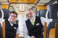 Eine Fahrgastbetreuerin und ein Fahrgastbetreuer sitzen in einem vlexx-Zug und lächeln