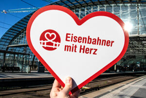 Eimi H Herz vlexx Startseite Logo auf Herz wird vor Bahnhof gehalten